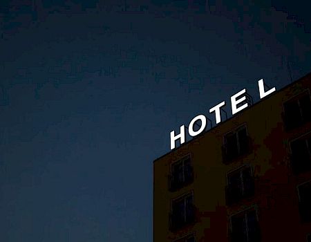 A building with a lit-up "HOTEL" sign at the top, seen against a dark sky.