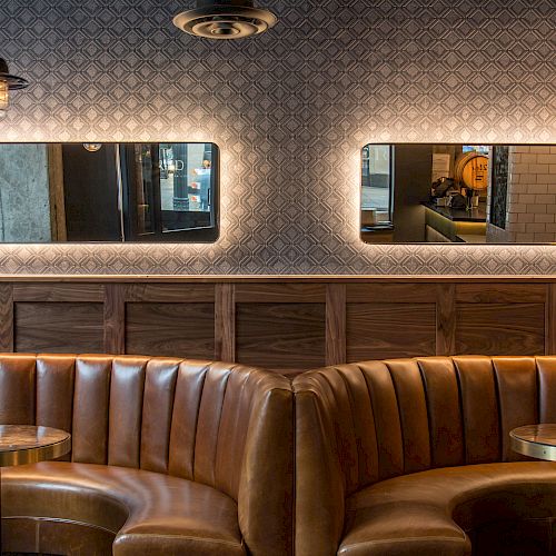 A chic, modern restaurant interior featuring leather booths, gold tables, pendant lights, and wall mirrors reflecting the outside view.