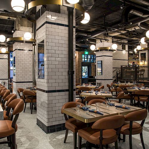 The image shows a modern restaurant interior with white-tiled pillars, brown chairs, tables set for dining, and spherical hanging lights.