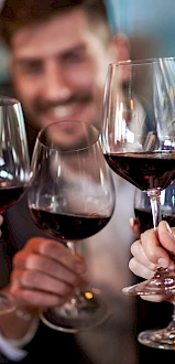 People are raising wine glasses in a toast, creating a celebratory atmosphere with smiles and blurred background lights.