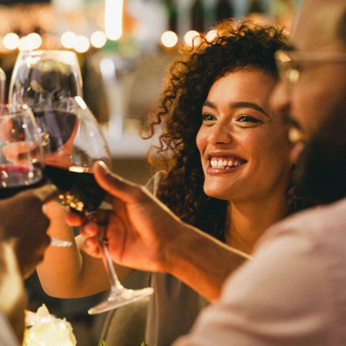 A group of people is clinking wine glasses in a celebratory toast, smiling and enjoying each other's company in a warm, festive setting.