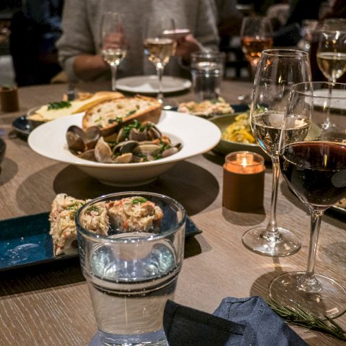 A table is set with plates of food, wine glasses, water glasses, and a lit candle. Multiple people are dining together, sharing a meal ending the sentence.