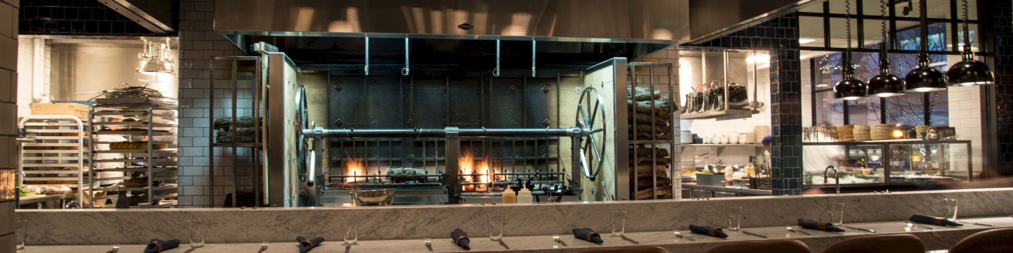 This image shows a restaurant kitchen with an open design, featuring bar seating and a visible cooking area with various kitchen equipment.