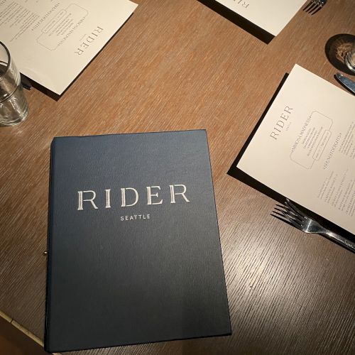 A table with menus labeled "RIDER" and cutlery set on wooden surface.