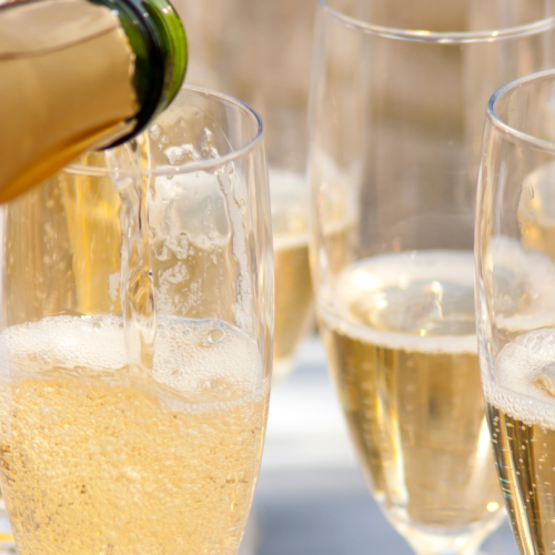 Several flutes filled with champagne, with one being poured from a bottle, creating bubbles in a celebratory setting.