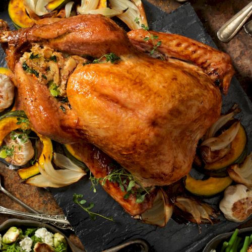 A roasted turkey with stuffing, surrounded by roasted vegetables, cranberries, and a variety of side dishes on a rustic table.